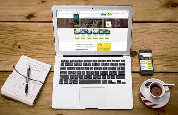 Macbook with desktop website open and iPhone with mobile website open on wooden table.