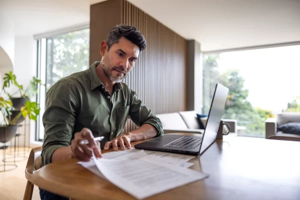 A contractor working from home, sat at a dining table working on a laptop