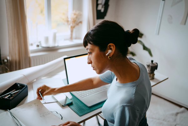 Someone working from home sat at a desk, with a computer and paperwork in front of them
